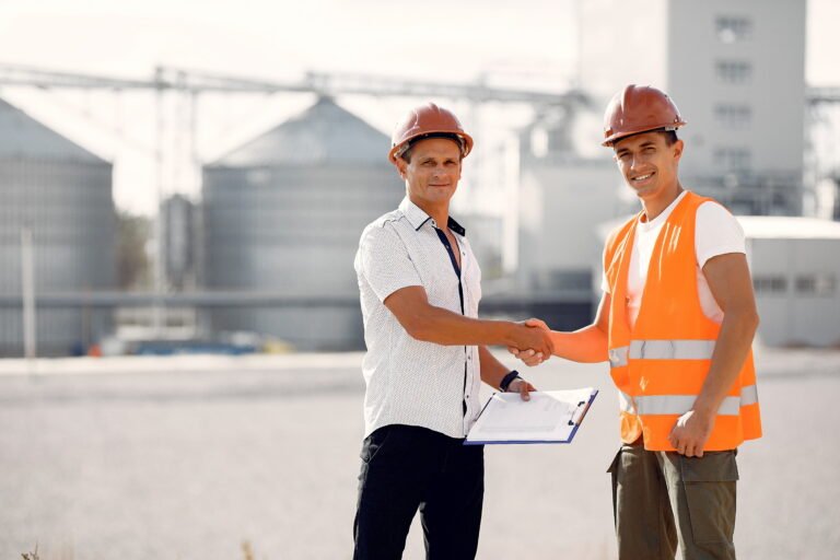 Engineers in hard hats shaking hands at an industrial project site